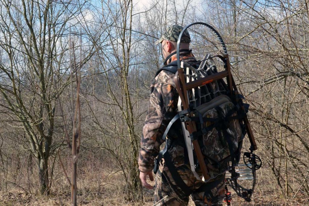 Hunter With Climbing Tree Stand Packed On Back